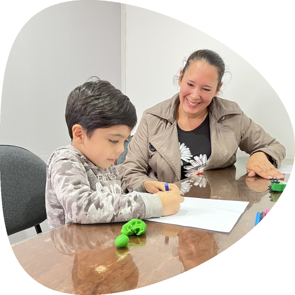 Una estudiante de psicologia realiza atencion a un paciente pediatrico que está trabajando en una hoja sobre una mesa.